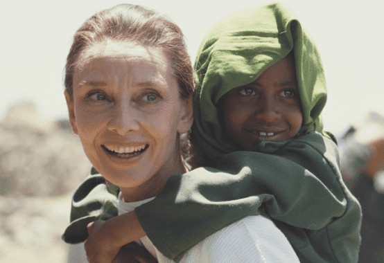 Audrey Hepburn is carring a African little boy. 